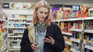 Woman looks at phone while holding a box of stock cubes in a grocery store