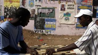 Des résidents de Bissau s'adonnent au jeu de dame devant un mur couvert d'affiches de partis politiques (illustration)