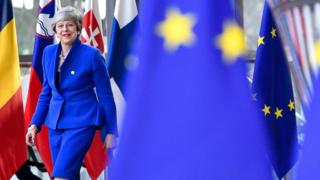 May caminha e sorri entre bandeiras da União Europeia e de países do bloco