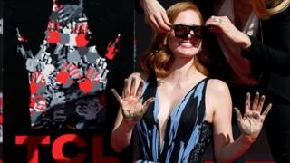 Actor Jessica Chastain is helped with her sunglasses after placing her hands in cement during a ceremony in the forecourt of the TCL Chinese theatre in Hollywood, Los Angeles, California