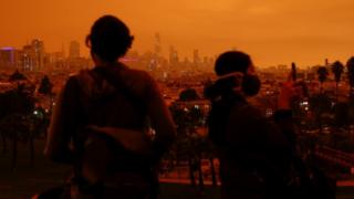 Visitors are seen in Dolores Park under an orange sky