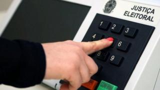 Pessoa aperta botão em urna eletrônica