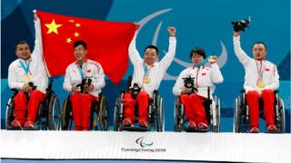 Curling competitors line up with their gold medal whilst waving a Chinese flag.
