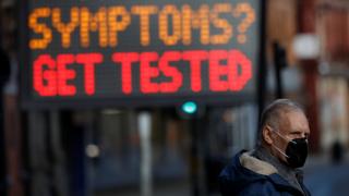 Man in mask stands next to sign in Bolton