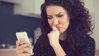 Mulher olha para celular com uma expressão de insatisfação