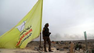 Fighter of the Syrian Democratic Forces (SDF) stands guard next to a yellow flag in Baghuz