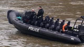 A police boat, with two officers on board, searches the River Thames near Chelsea Bridge