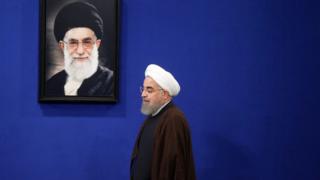 Newly re-elected Iranian President Hassan Rouhani walks past a picture of Iranian Supreme leader Ayatollah Ali Khamenei