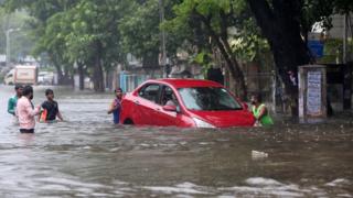 People help a woman to move her car through a water-logged road during rains in Mumbai, August 29, 2017