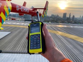 A hand holds a phone device with an air ambulance in the background