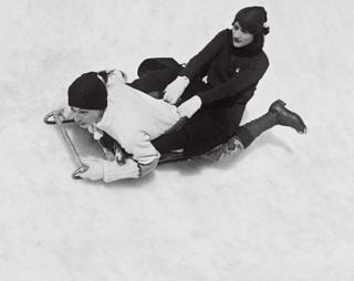 A young man and woman fly sledge down a snow-covered slope