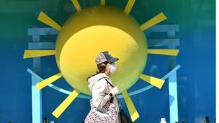 A woman wearing a face mask as a precaution walks past a window display at Selfridges on Oxford Street in London on May 2.