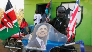 A Kenyan man sitting on a motorbike decorated with a poster of Barack Obama and the Kenyan and US flags, Kogelo, Kenya - Monday 16 July 2018