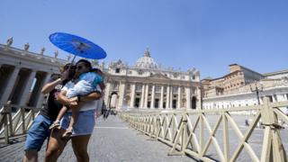 Ein Paar mit einem Kind versucht, sich mit einem Sonnenschirm vor der Sonne zu schützen, während es in der Nähe des Vatikans spazieren geht
