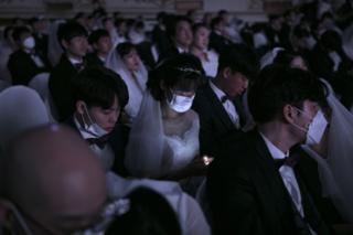 A bride, wearing a mask, checks her phone during a mass wedding ceremony organised by the Unification Church in Gapyeong