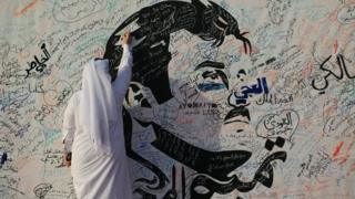 A man writes on a painting depicting Qatar's Emir Sheikh Tamim Bin Hamad Al-Thani in Doha, Qatar, 2 July 2017