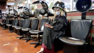 A customer wearing a face mask sits under a dryer at an empty salon in Marietta, Georgia