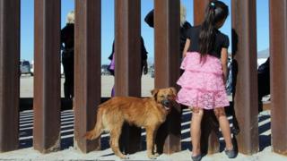 Menina olha pela grade que separa EUA do México