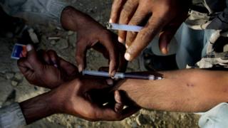 A man injects heroin into a fellow addict's arm in Quetta, Pakistan.
