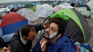 Мигрант бреет другого во временном лагере на греко-македонской границе, недалеко от греческой деревни Идомени