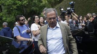 Paulo Guedes caminha em rua cercado por jornalistas