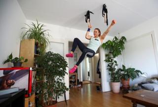 A climber dangles from handles in the ceiling of her living room