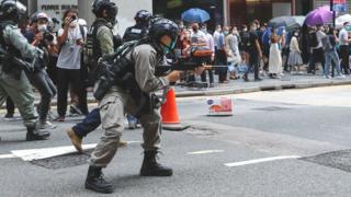 A riot police officer fires his weapon during a protest in Central,