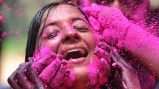 Hands rub pink paint powder on a girl's face
