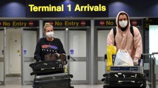 Passengers wearing PPE (personal protective equipment), including a face mask as a precautionary measure against COVID-19, arrive at Terminal 1 of Manchester Airport