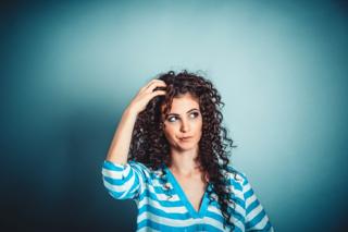 Portrait close-up of a woman wearing a blue and white stripy top, she's looking up, confused, and is standing in front of a blue wall background