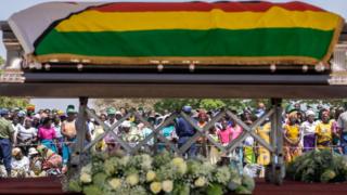 Villagers look at the coffin of late former Zimbabwean president Robert Mugabe lying in state at Murombedzi Growth Point, about 107 km northwest of Harare, Zimbabwe, on September 16, 2019, as people have been accorded the opportunity to view Mugabe's body a week after his death. - The remains of former Zimbabwe president Robert Mugabe were taken to his village for a wake on September 16, a family member said, as his final burial is prepared in about a month. Mugabe died a week ago aged 95 in Singapore, nearly two years after he was ousted in a 2017 coup that ended nearly four decades of increasingly autocratic rule. After a state funeral on September 14 in the capital Harare attended by African leaders, his body went to his rural village of Kutama, 90 kilometres (55 miles) to the west, to allow villagers to pay tribute and bid farewell.