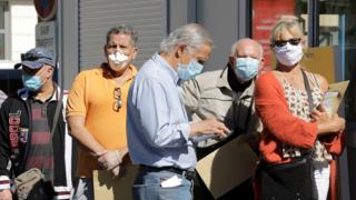People wearing protective face masks queue at a post office in Mandelieu, France