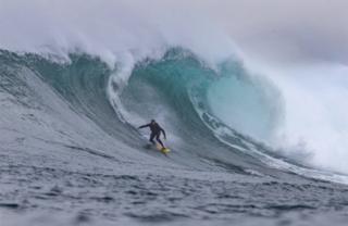 A surfer rides under the crest of a wave.