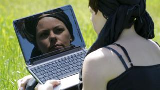 Женщина смотрит на свое отражение в компьютере