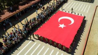 An aerial view of Turkish soldiers parading with a massive Turkish flag