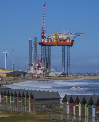 A coastal view of beach huts and an industrial structure