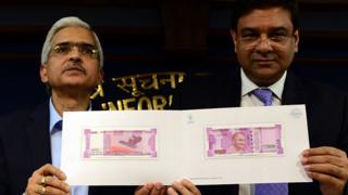 Шактиканта Дас и бывший управляющий Резервного банка Индии Урджит Р. Патель держат образец новой банкноты в 2000 рупий на пресс-конференции в Нью-Дели