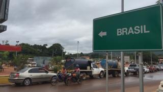 Fila de vehículos y un cartel que indica la dirección a Brasil