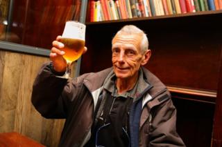 A man holds his pint of beer up to the camera