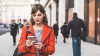 mujer usando teléfono móvil caminando por la calle.