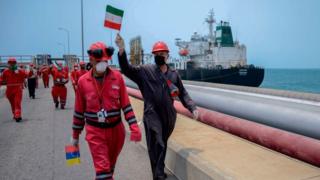 عامل في شركة النفط الفنزويلية الحكومية يلوح بالعلم الإيراني بينما ترسو ناقلة النفط فورتشن التي ترفع العلم الإيراني في مصفاة إل باليتو في بويرتو كابيلو، في ولاية كارابوبو الشمالية، فنزويلا، في 25 مايو/أيار 2020