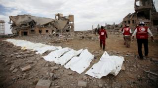 Red Crescent medics walk next to bags containing the bodies of victims of Saudi-led airstrikes on a Houthi detention centre in Dhamar, Yemen,