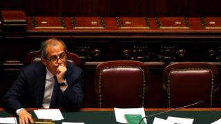 Italian Economy Minister Giovanni Tria, pictured alone, muses in Italy's dark oak and red leather parliament chamber