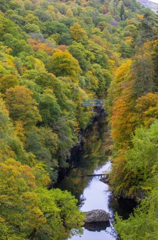 Warna-warna hijau, merah dan kuning terpantul dari pepohonan di sisi jembatan River Barry dekat desa Killiecrankie in Perthshire