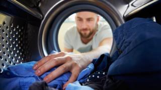 Мужчина кладет руку в стиральную машину