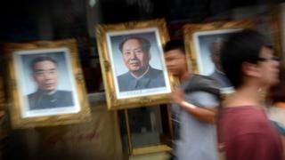 People walk past a portrait of Mao Zedong
