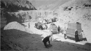 Team of archaeologists and assistants transporting crates on rails through rocky hills