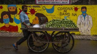 Vendor in New Delhi walks past a mural with doctors and people wearing masks