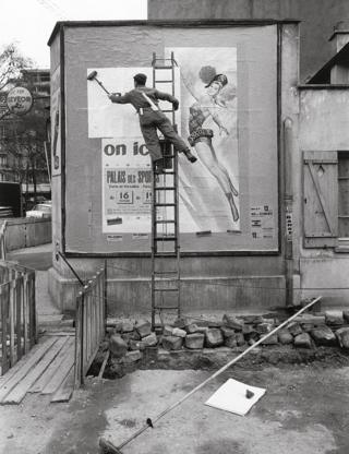 man stands on a ladder and puts up a billboard poster
