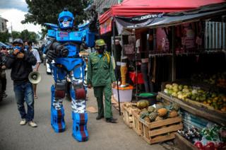 A man wearing a Transformers costume walks past a food stall